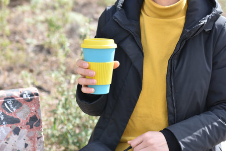 one girl sitting outdoors holding coffee cup , take away coffee.
