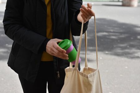 Female hands holding reusable coffee cup putting into a bag outdoors.の写真素材