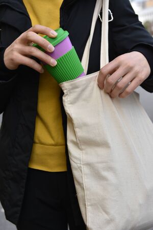 Female hands holding reusable coffee cup putting into a bag outdoors.の写真素材