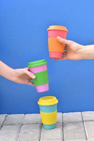 hands of two girls taking eco coffee cup on blue background, take away coffee.Breakfast on the go.Sustainable lifestyle concept.Top view flat layreusable travel mug. Zero waste. の写真素材
