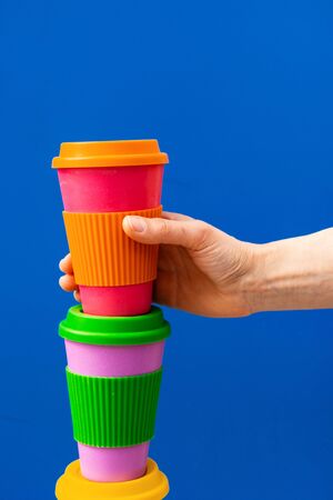 One woman's hand taking eco coffee cup. Zero waste concept. Make a choice.Take away coffee outdoors lifestyle.Copy space for texture on blue background. の写真素材