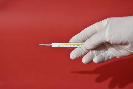 Hand in white medical glove holds medical mercury thermometer.Defocused photo.の写真素材