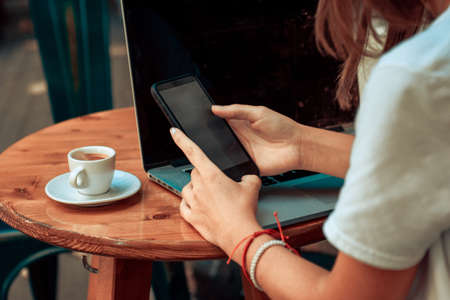 woman sitting at wooden table in cafe using laptop and mobile phoneの写真素材