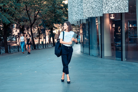 Business woman with laptop and smart phone in hands on city street.