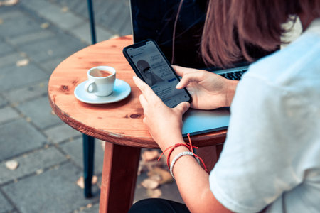 woman sitting at wooden table in cafe using laptop and mobile phone