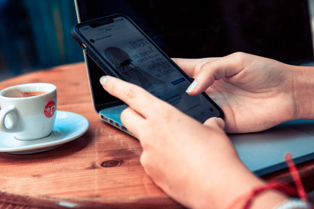 woman sitting at wooden table in cafe using laptop and mobile phone