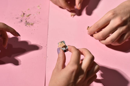 Hand holding pencil sharpener and pencil shavings on pink background.の写真素材