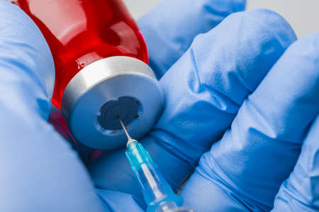 Hand in medical glove picking medication into the syringe from red ampouleの写真素材
