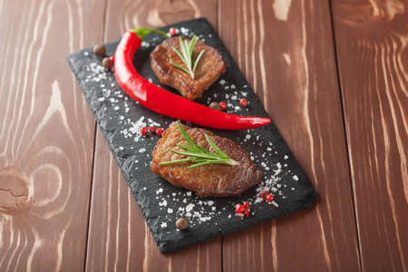 grilled steak with rosemary and chili peppers on wooden backgroundの写真素材