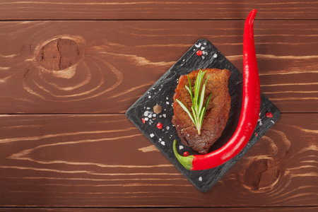 grilled steak with rosemary and chili peppers on wooden backgroundの写真素材