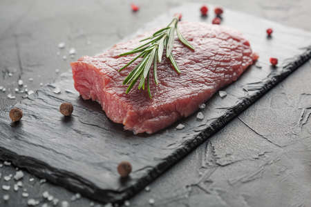 raw beef steak with rosemary and peppers on dark stoneの写真素材
