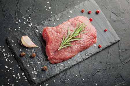 raw beef steak with rosemary and peppers on dark stoneの写真素材