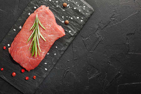 raw beef steak with rosemary and peppers on dark stoneの写真素材