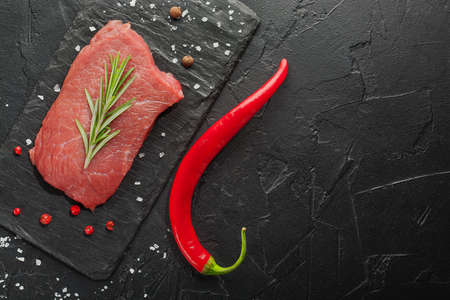 raw beef steak with rosemary and peppers on dark stoneの写真素材