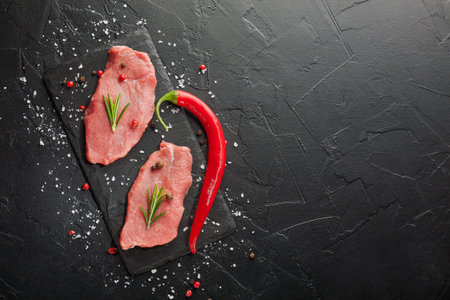 raw beef steak with rosemary and peppers on dark stone