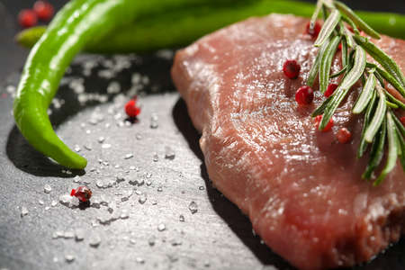 raw beef steak with rosemary and peppers on dark stoneの写真素材