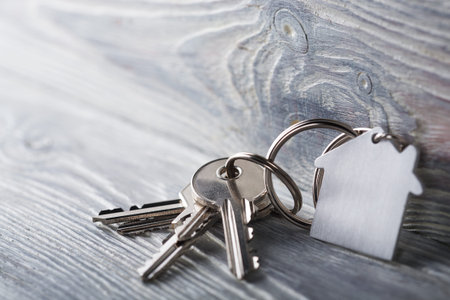 Keys to house with keychain on white wooden background