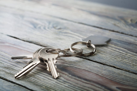 Keys to house with keychain on white wooden background