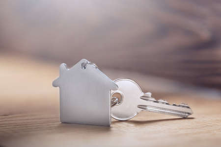 House key on house shaped keychain on wooden floorboardsの写真素材