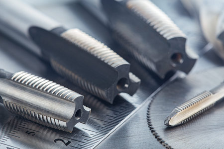 set of different drill bits, thread taps and mill cutters with ruler on steel plate background....