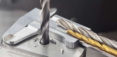 drill bit make holes in steel billet on industrial drilling machine with ruler and caliper. Metal work industry. multi cutting tool and end mill.の写真素材