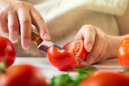 Chef slicing tomato using knife on the table in restaurant. Process of cutting and preparation food...