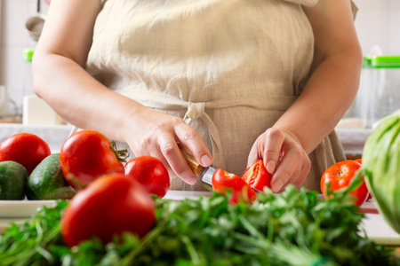 Chef slicing tomato using knife on the table in restaurant. Process of cutting and preparation food in kitchen.の写真素材