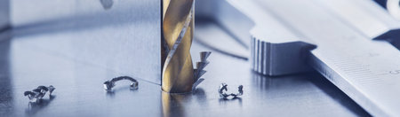 metal drill bit with triangle ruler make holes in steel billet on industrial drilling machine. Metal...