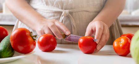 Chef slicing tomato using knife on the table in restaurant. Process of cutting and preparation food in kitchen.の写真素材