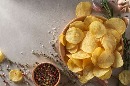 Pile of crispy potato chips in bowl on a concrete table with spices in kitchen. Concept of fast food background. Free place for text, top view.の写真素材