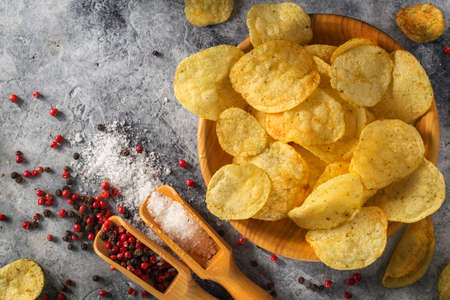 Chips, potato crisps heap with garlic, rosemary, in bowl on gray stone background. Junk food or fast food.の写真素材