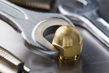 Wrench tightens brass cap nut in steel billet. Spanner, bolt, screw and nuts.の写真素材