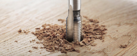 Thread tap drill cutting hole in wooden plate. working cutter.