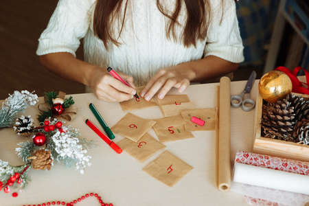 a table with Christmas decorations and the hands of a girl writing numbers on an advent calendar diyの写真素材