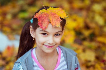smiling beautiful girl with brown eyes with maple leaf on her headの写真素材