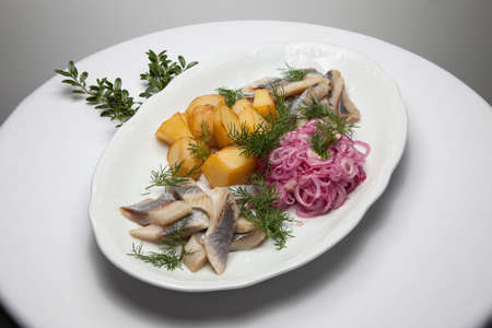Slices of salted herring with boiled potatoes, onions and dill on a white plate, traditional Russian appetizerの写真素材