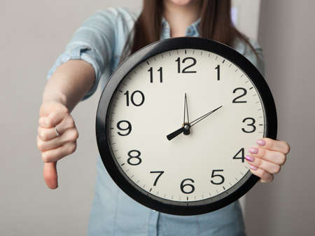 The girl with a clock the large clock in the background of girls, which keeps them in one hand while the other hand shows dislike or thumb downの写真素材