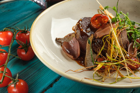Warm meat salad with tongue on a light plate decorated with vegetables, cherry tomatoes and edible...