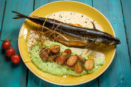 Mackerel baked to a Golden crust with fried potatoes in pesto sauce on an orange plate standing on a blue wooden backgroundの写真素材