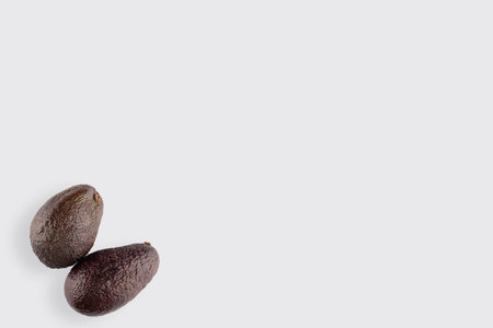 two Australian Hass avocados close up in the lower left corner of the white background