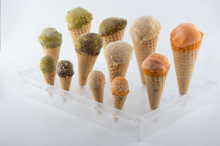 organic handmade ice cream cones in four flavors and different sizes on a stand. The flavors are chocolate, pistachio, caramel and mango. Close upの写真素材