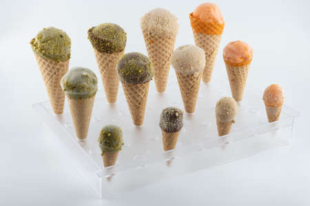organic handmade ice cream cones in four flavors and different sizes on a stand. The flavors are chocolate, pistachio, caramel and mango. Close upの写真素材
