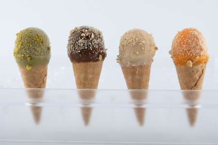 organic handmade ice cream cones in four flavors and different sizes on a stand. The flavors are chocolate, pistachio, caramel and mango. Close upの写真素材
