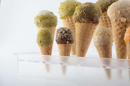 organic handmade ice cream cones in four flavors and different sizes on a stand. The flavors are chocolate, pistachio, caramel and mango. Close upの写真素材