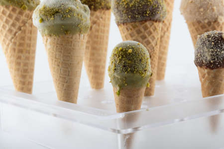 organic handmade ice cream cones in four flavors and different sizes on a stand. The flavors are chocolate, pistachio, caramel and mango. Close upの写真素材
