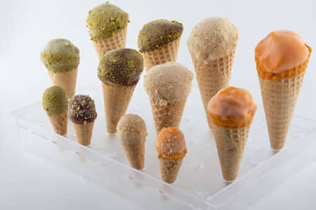 organic handmade ice cream cones in four flavors and different sizes on a stand. The flavors are chocolate, pistachio, caramel and mango. Close upの写真素材