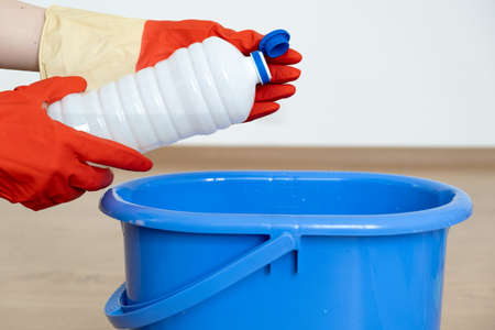 Hands in gloves for cleaning pour a cleaner for cleaning surfaces over a blue bucket.の写真素材
