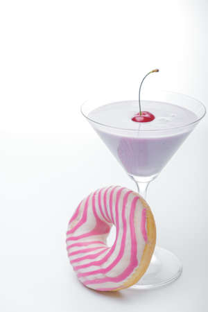  a glass of martini and a pink and white striped donut close-up. photo for the screensaver. In a glass of milkshake milkshake. One cherry on top.の写真素材