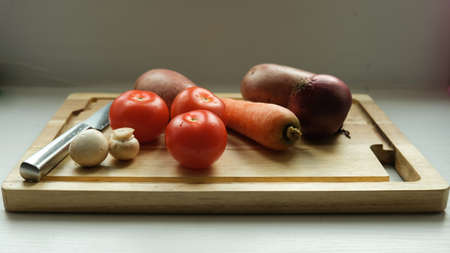  vegetables on a cutting board. Close-up of tomato, potato, mushrooms and carrots. And in the background is a knife.の写真素材
