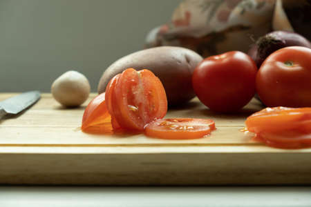  vegetables on a cutting board. close-up sliced ââtomato, and in the background potatoes, mushrooms and carrots. の写真素材